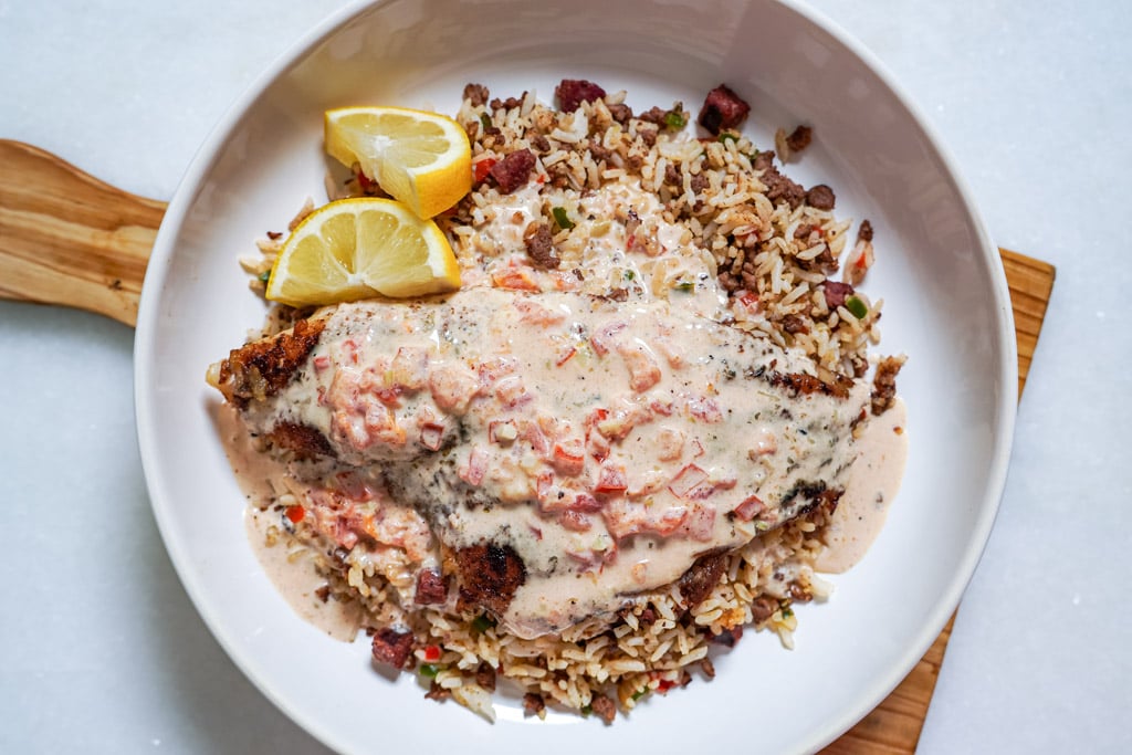 blackened catfish with a cream sauce in a bowl over a bed of dirty rice