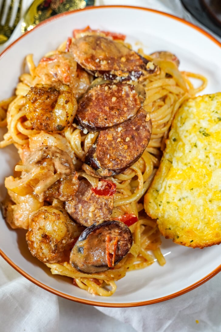 Cajun pasta plated on a white plate with a side of garlic toast