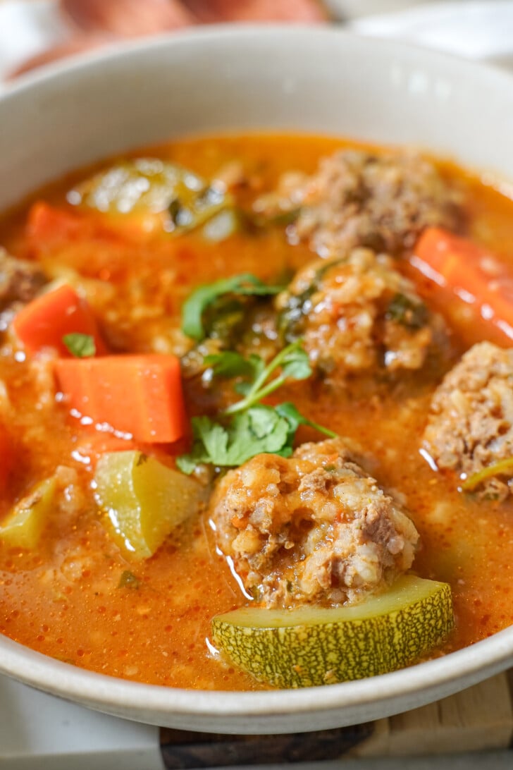 a close-up of albondigas soup in a white bowl
