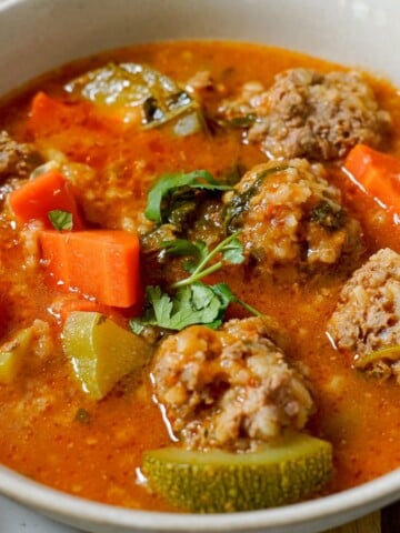 a close-up of albondigas soup in a white bowl
