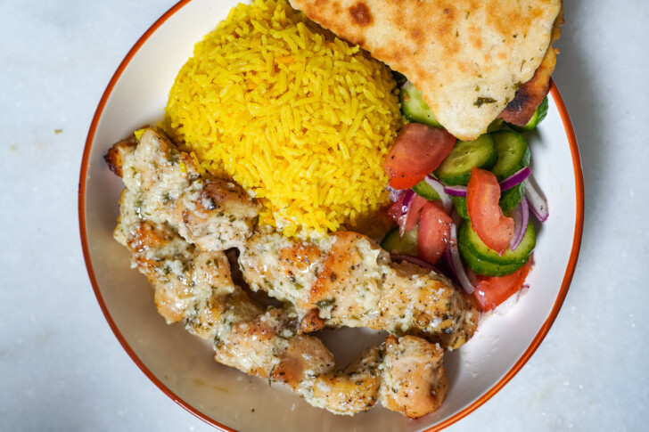 chicken kabobs in a bowl with rice and a small salad