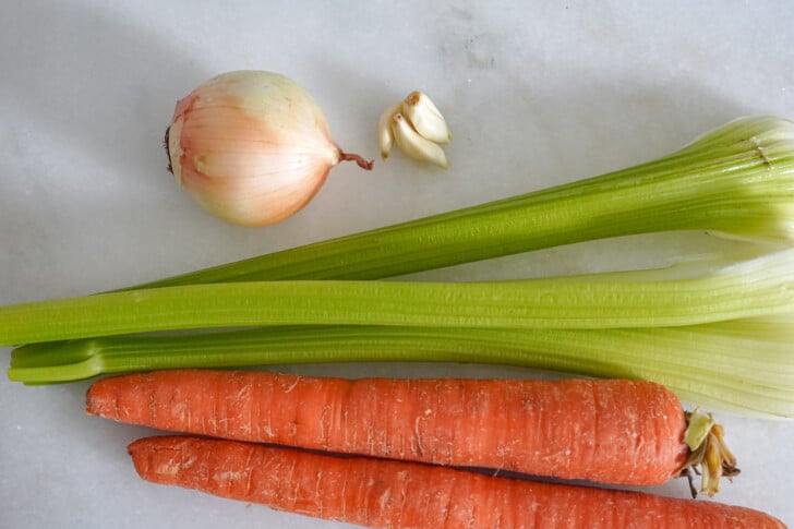 carrots, celery, onion, and garlic on a white countertop