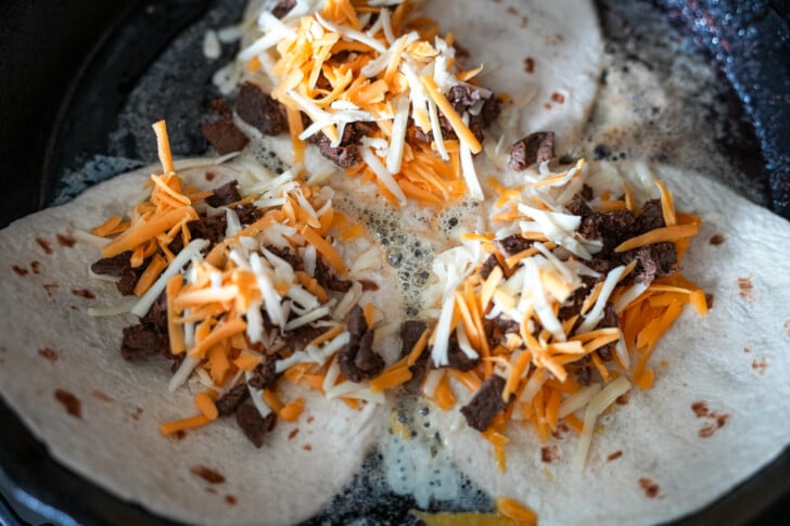 shredded cheese and steak meat on a tortilla in a skillet