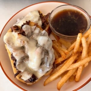 roast beef sandwich on a plate with french fries and au jus sauce