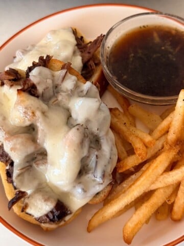 roast beef sandwich on a plate with french fries and au jus sauce