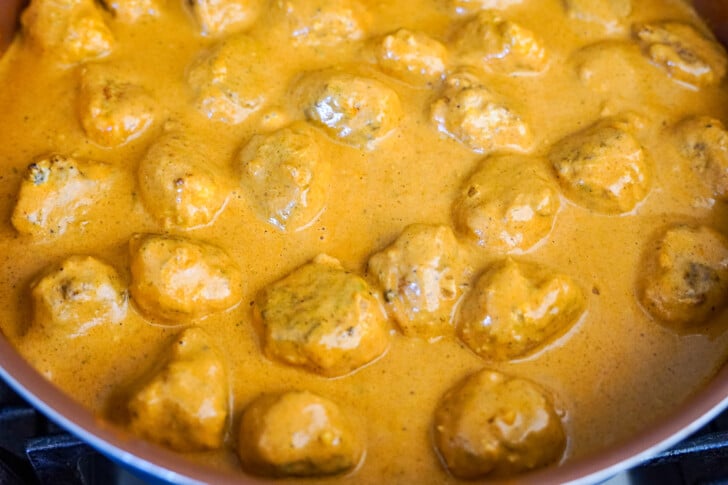 meatballs simmering in a skillet with butter chicken sauce.